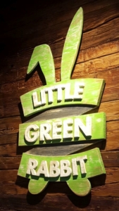 Little Green Rabbit wooden wall sign showing the logo. Green rabbit ears on top, underneath three green stripes displaying "Little Green Rabbit".