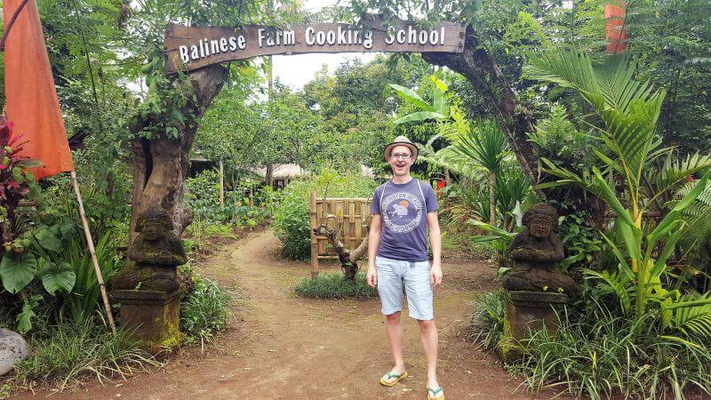 Pemula Bali Farm Cooking School. Ich stehe am Eingangstor. Auf dem Balken darüber steht: Balinese Farm Cooking School