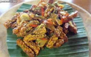 Bali Farm Cooking. Sweet and sour tempe. Fride tempe with vegetables served on a banana leaf on a wooden plate.
