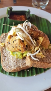 Bali Buda. Breakfast. Avocado Smash vegan version with crispy tofu. Toast cut in half stacked on a banana leaf topped with avocado, sprouts and fried tofu.