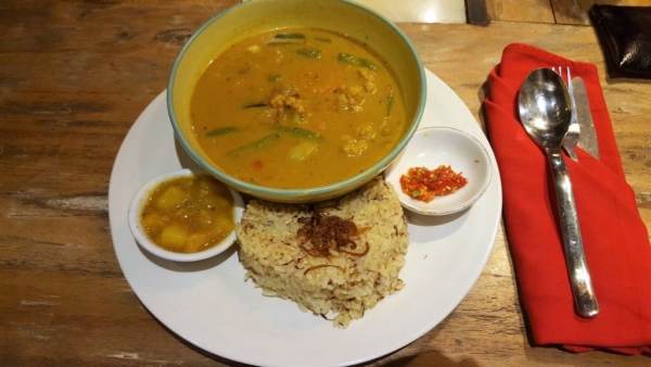 Eating out in Ubud. Clear Café. Vegetable Curry. Golden Temple Curry in a bowl on a large plate on which you see a portion of rice in form of a heart and two little bowls with chutneys.