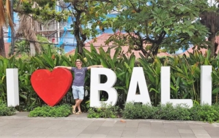 I love Bali. Foto von mir zwischen den mannshohen Buchstaben weißes I, rotes Herz und BALI in weiß auf einem Parkplatz in Seminyak.