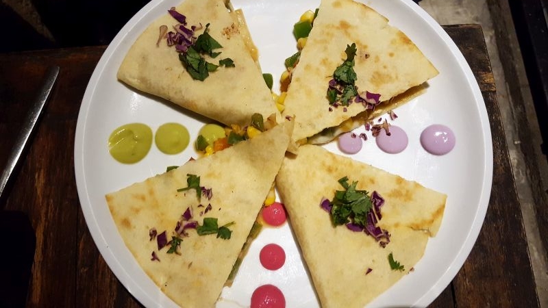 Eating out in Ubud. Lazy Cats. Cheeseadilla. Quesadillas on a plate, between the different segments there are colored dots of sauce.