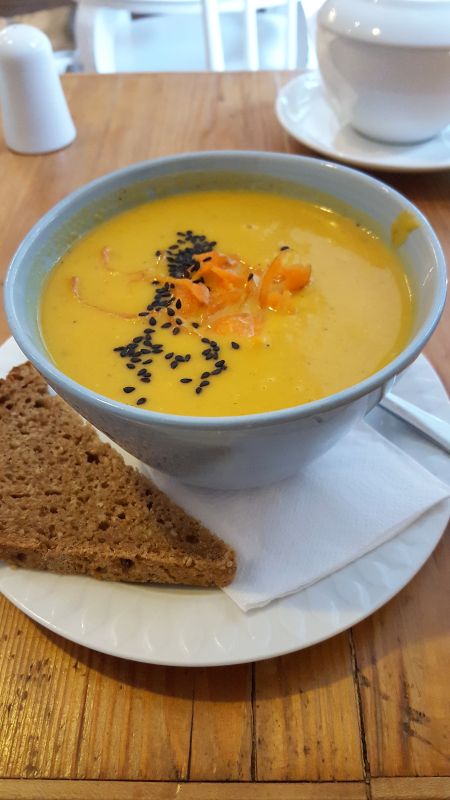 Café con amore. Peanut-carrot-soup served in a bowl and with a slice of whole grain bread decorated with black sesame and thin carrot slices.