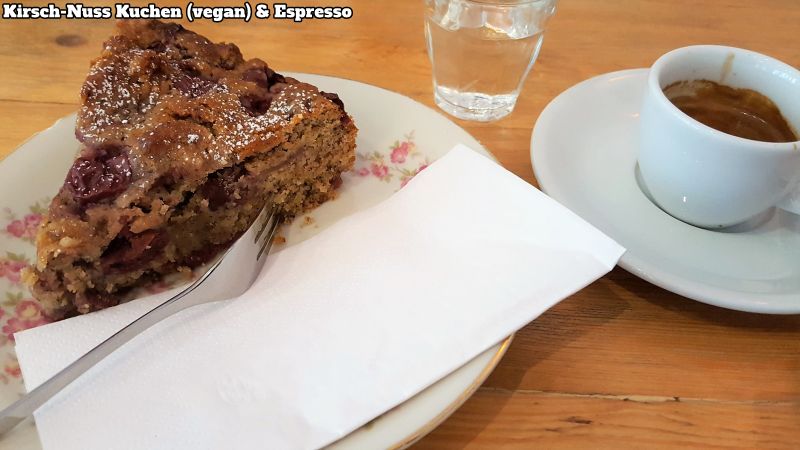 Veganer Kirsch-Nuss-Kuchen und ein Espresso, dazu ein Gläschen Wasser.
